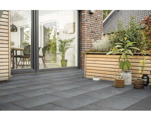 Moderne Terrasse mit grossformatigen Plattenbelag aus Feinsteinzeug, angrenzend an eine Holzfassade mit Hochbeet und raumhoher Verglasung.