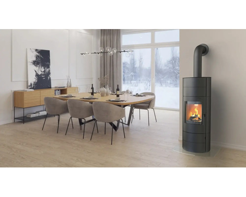 Poêle à bois moderne dans une salle à manger lumineuse avec table en bois et chaises devant une baie vitrée donnant sur un paysage enneigé.