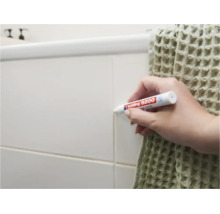 Personne utilisant un feutre à joints Edding 8200 pour rafraîchir les joints de carrelage sur un mur de salle de bain.