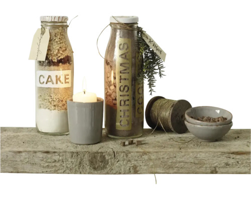 Deux bouteilles en verre avec des préparations pour gâteaux, une bougie dans un pot, une bobine de fil et des petits bols sur une planche en bois.