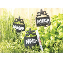 Trois étiquettes de plantes rustiques en métal avec inscription parmi des herbes fraîches et un marqueur Edding pour surfaces lisses.