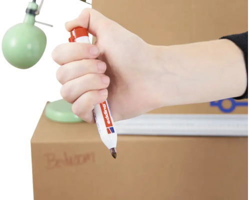 Hand hält einen Edding Permanentmarker zum Beschriften eines Kartons