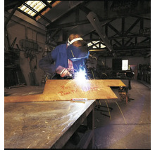 Un soudeur travaille sur une plaque métallique avec un marqueur Edding dans un atelier industriel.