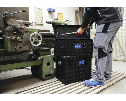 Handwerker mit Alutec Werkzeugkiste aus Aluminium Riffelblech in einer Werkstatt neben einer Drehmaschine.