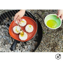 Person beträufelt auf einem Grill stehenden Grillkäse in einer Keramikpfanne mit Öl. (Image AI modified or generated)
