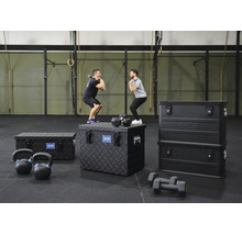 Drei schwarze Aluminiumboxen von Alutec Munchen auf dem Boden eines Fitnessstudios mit Sportgeräten wie Kurzhanteln und zwei trainierenden Männern.