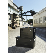 Zwei schwarze Aluminium Transportboxen von Alutec mit einem Bauhelm auf dem Werksgelände im Freien.