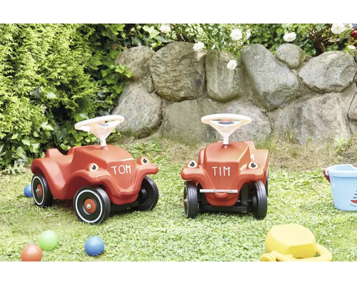 Zwei Rutschautos aus Kunststoff fur Kinder in einem Garten mit Natursteinmauer.