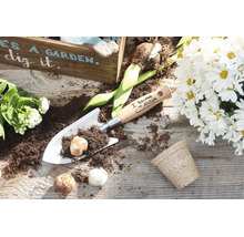 Personalisierte Handschaufel aus Metall mit Holzgriff und Blumenzwiebeln auf einem Holztisch mit Pflanzenarrangement.