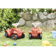 Zwei Rutschautos aus Kunststoff fur Kinder in einem Garten mit Natursteinmauer.