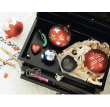Une boîte à outils noire ouverte contenant plusieurs boules de Noël décoratives et deux marqueurs Edding pour la décoration.