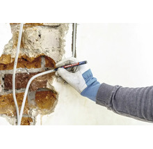 Eine Hand mit Schutzhandschuh beschriftet ein Stromkabel auf einer verputzten Mauer mit einem Edding 8407 Kabelmarker.