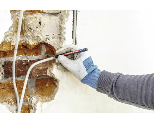 Eine Hand mit Schutzhandschuh beschriftet ein Stromkabel auf einer verputzten Mauer mit einem Edding 8407 Kabelmarker.