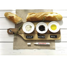 Un marqueur craie edding posé sur une planche en bois avec des bols étiquetés pour le sel, les olives et l'huile à côté d'une baguette.