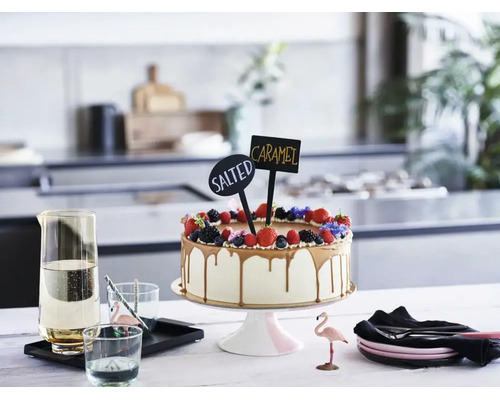Gâteau décoré de baies et de panneaux avec inscription Salted Caramel sur un présentoir dans une cuisine moderne