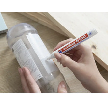 Une main utilise le stylo dissolvant d'étiquettes Edding 8180 pour enlever une étiquette d'une bouteille en plastique.