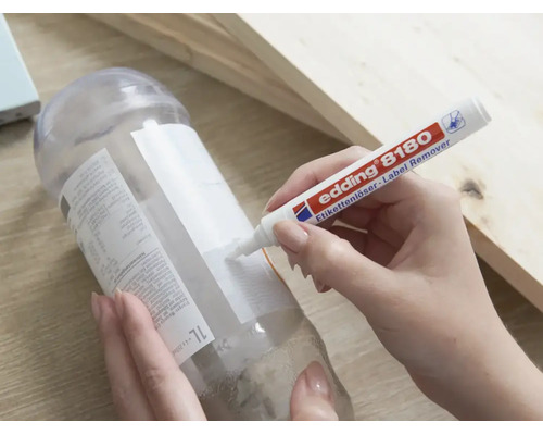 Une main utilise le stylo dissolvant d'étiquettes Edding 8180 pour enlever une étiquette d'une bouteille en plastique.