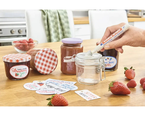 Stylo dissolvant d'étiquettes Edding 8180 utilisé pour enlever les résidus de colle d'un pot vide, entouré de pots de confiture et de fraises.