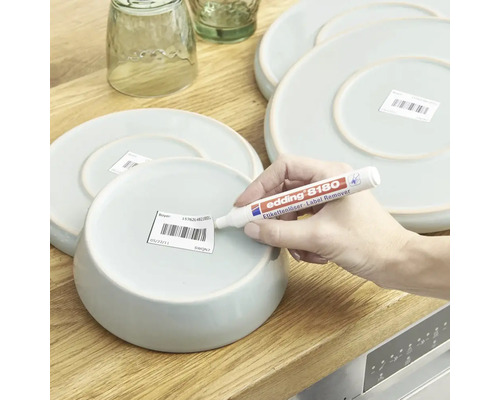 Une personne utilise un stylo dissolvant d'etiquettes Edding 8180 pour enlever une etiquette sous un bol en ceramique.