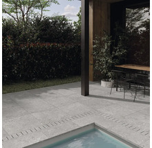 Terrasse mit grauen Steinoptik Fliesen um einen Pool, angrenzend an ein modernes Haus mit Sitzbereich im Außenbereich.
