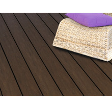 Lames de terrasse en bois foncé avec un fauteuil tressé en osier et un coussin violet sur une terrasse.
