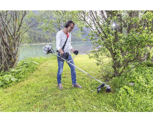 Mann mit Kopfhörern mäht Gras mit einem Trimmer am See