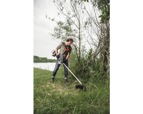 Mann benutzt einen Rasentrimmer im Garten, um das Gras zu schneiden.