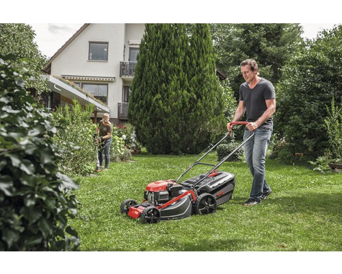 Un homme tond la pelouse avec une tondeuse à gazon dans un jardin