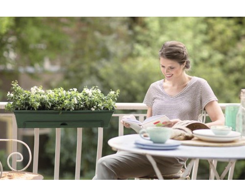 Frau liest auf dem Balkon mit Balkonkasten und Tischgedeck