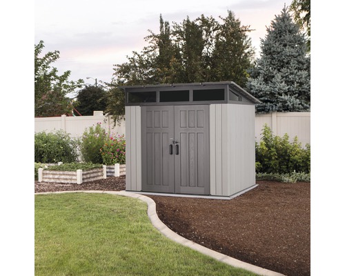 Abri de jardin avec double porte et lucarne dans un jardin bien entretenu.