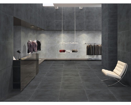 Intérieur avec carrelage gris au sol et aux murs, un fauteuil blanc et des vêtements sur des cintres