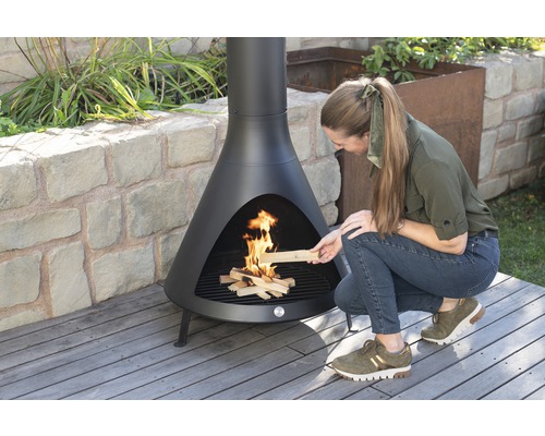 Frau legt Holz in eine schwarze Gartenfeuerstelle