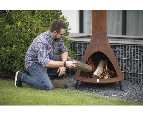 Mann legt Holz in einen Rost-farbenen Gartenkamin.