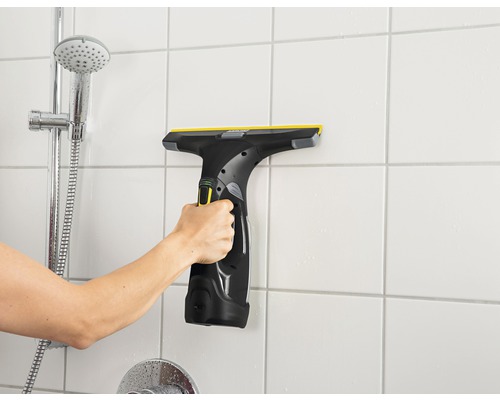 Main utilisant un aspirateur de vitres sur le carrelage mural de la salle de bains