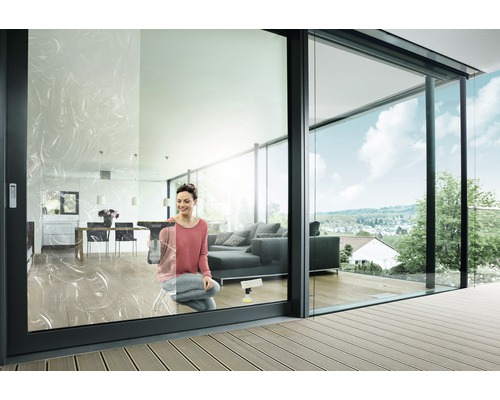 Femme nettoie les fenêtres dans un salon moderne avec des portes coulissantes en verre et une terrasse.