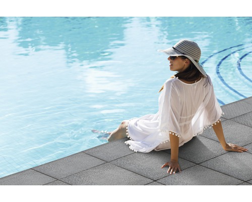 Femme assise au bord de la piscine sur des dalles de terrasse en pierre grise