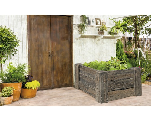 Garten mit Hochbeet aus Holz, Pflanzen und Gartengeräten vor einer Holzwand