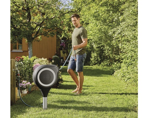 Scène de jardin avec un dévidoir et un homme tenant un tuyau d''arrosage.
