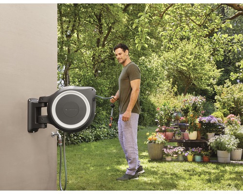 Un homme utilise un boîtier de tuyau d''arrosage mural dans un jardin.