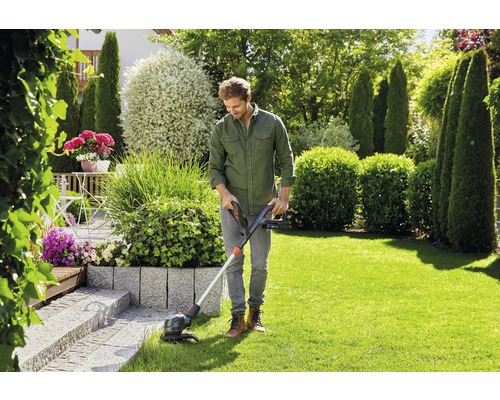 Un homme utilise un coupe-bordure dans un jardin avec une pelouse et diverses plantes.