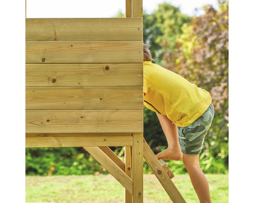 Un enfant grimpe sur une cabane en bois avec une échelle