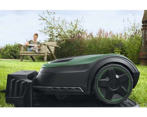 Robot tondeuse Bosch sur gazon avec femme sur un banc de jardin en arrière-plan