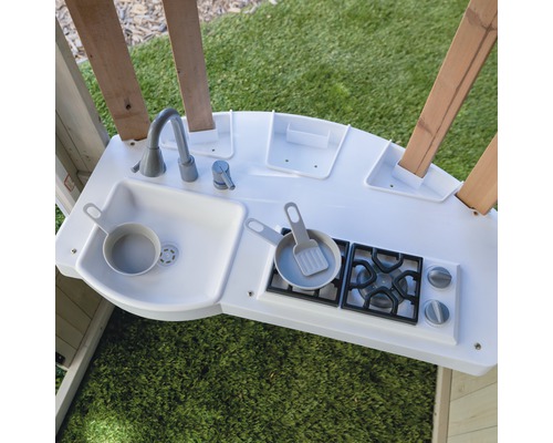 Cuisine pour enfants avec évier, cuisinière et vaisselle jouet sur une pelouse verte.