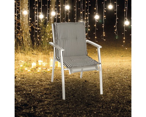 Chaise de jardin avec coussin rayé devant une guirlande lumineuse