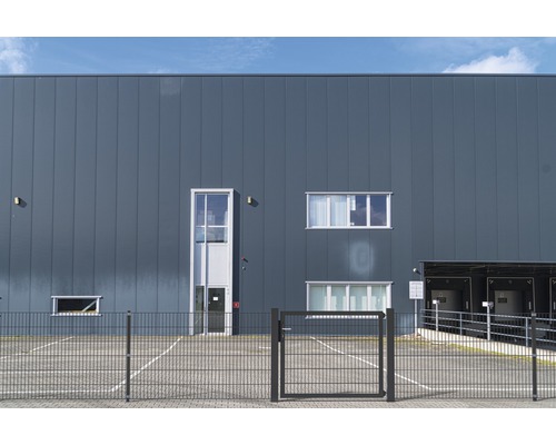 Aussenansicht eines Industriegebäudes mit Parkplatz und Zaun