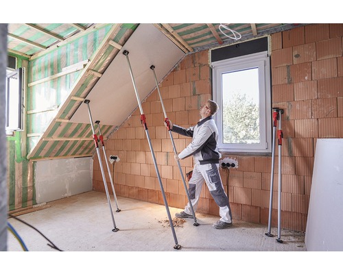 Ein Handwerker montiert eine Gipskartonplatte mit Teleskopstützen in einem Dachgeschossausbau.
