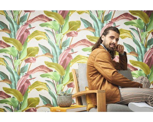 Ein Zimmer mit einer tropischen Blättertapete und einer Person, die auf einem Stuhl sitzt