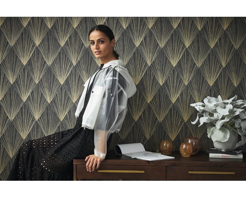 Scène avec papier peint à motifs et une femme assise sur un bureau avec une plante, des vases et des livres.
