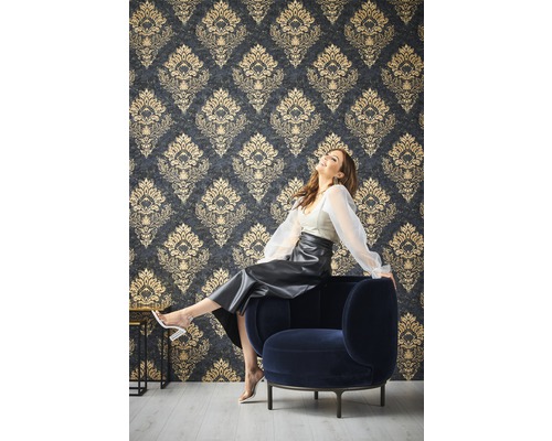 Femme assise sur un fauteuil devant un mur avec du papier peint à motifs