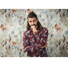 Homme avec une chemise à fleurs devant un mur endommagé